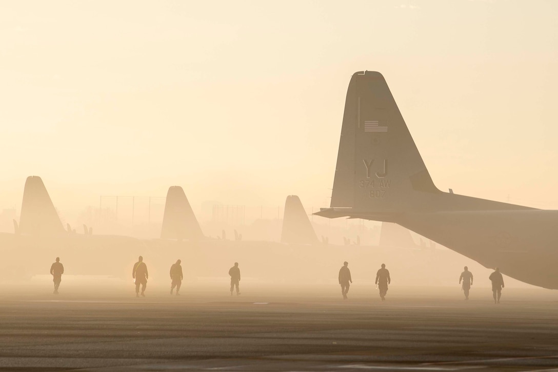 Airmen walk through the fog with aircraft sitting on the runway.