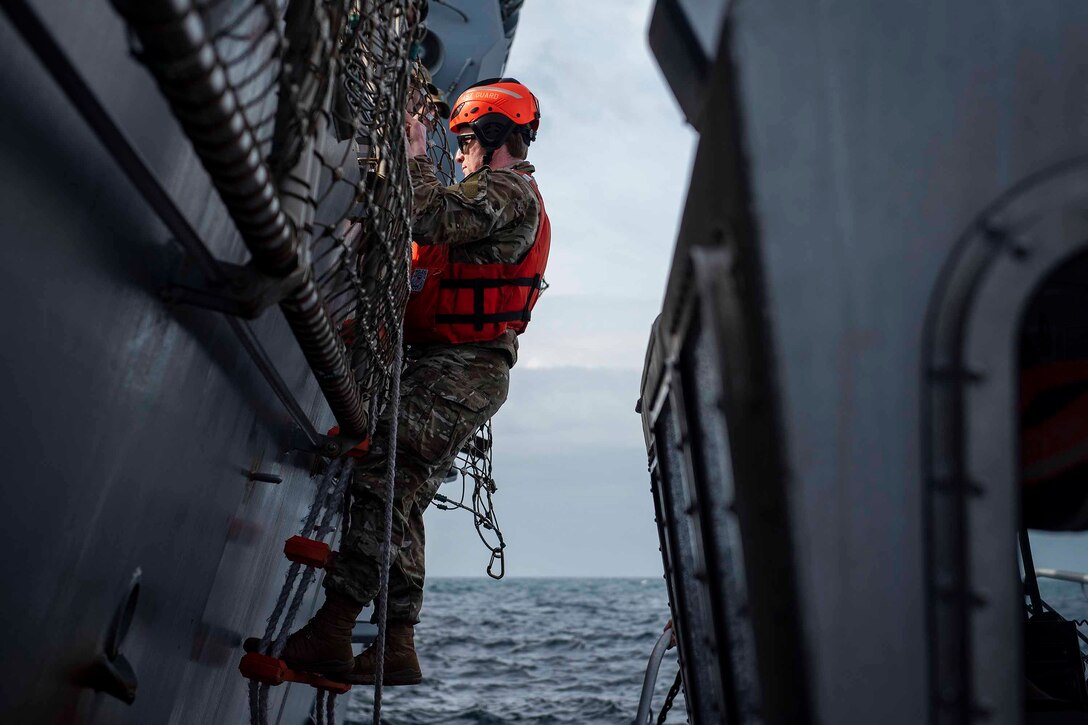An airman climbs a ladder on the side of a ship.