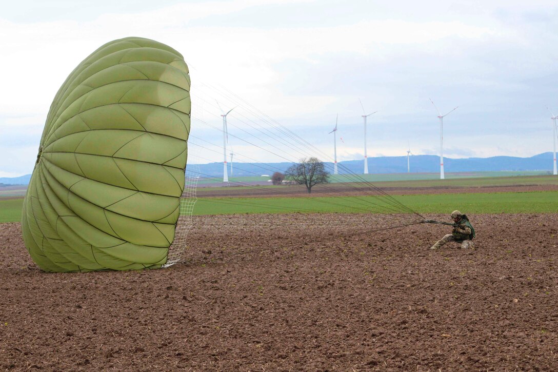 A soldier kneels on the ground holding onto an open parachute.