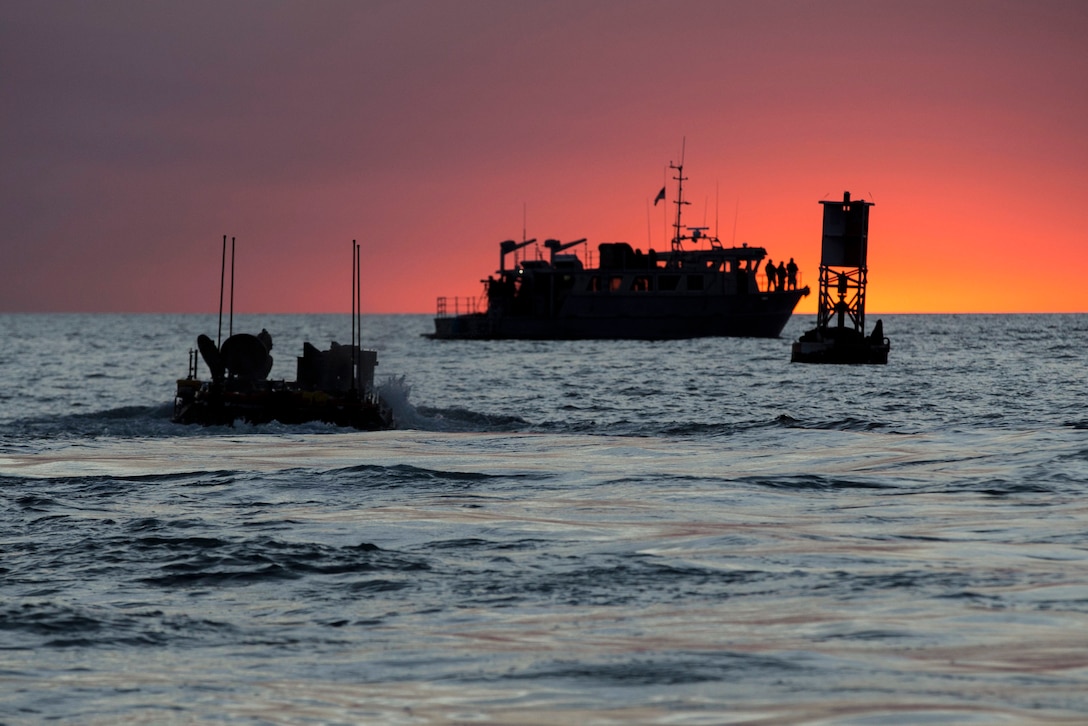 Three vessels, shown in silhouette, travel in water against a pinkish-purple sky.
