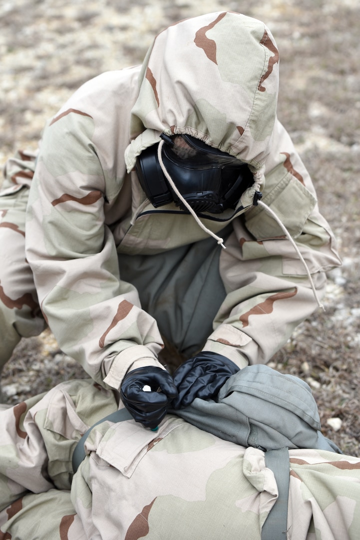 A Soldier wearing Mission Oriented Protective Posture, or MOPP, protective gear simulates using a CBD auto-injector device on a casualty during a field test  at Joint Base San Antonio-Camp Bullis