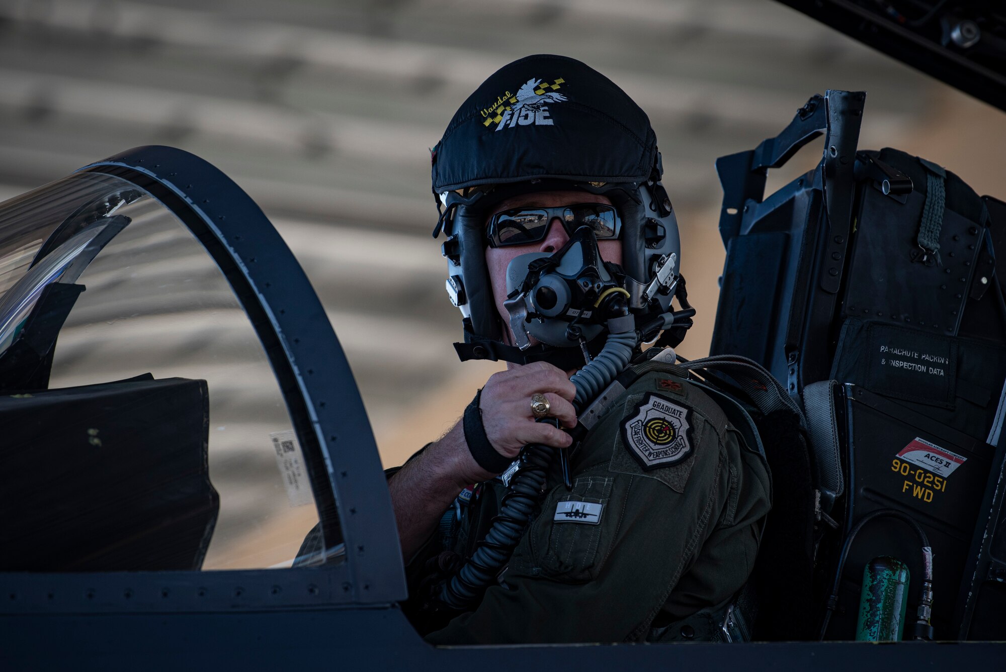 A pilot adjusts his oxygen mask in the cockpit of an F-15E Strike-Eagle fighter jet.