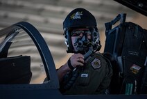 A pilot adjusts his oxygen mask in the cockpit of an F-15E Strike-Eagle fighter jet.
