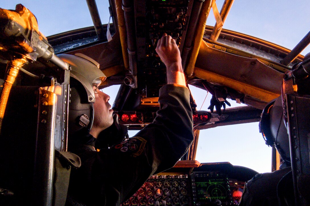An airman adjusts a knob above his head in the cockpit while flying an aircraft.