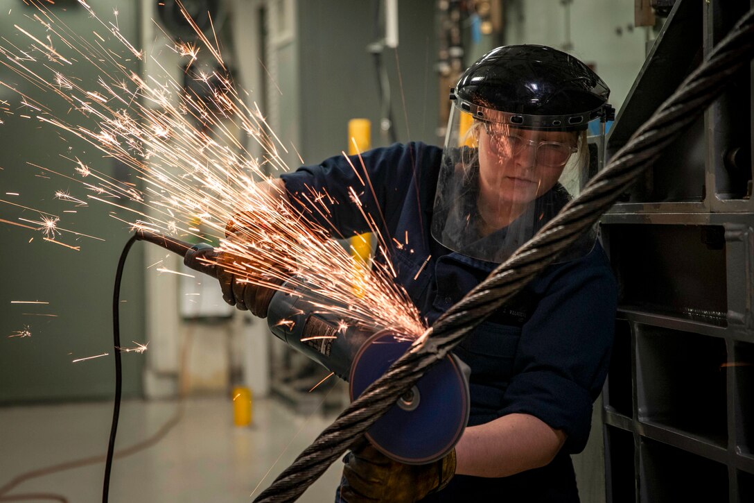 Sparks fly as a sailor welds a cable aboard a ship.