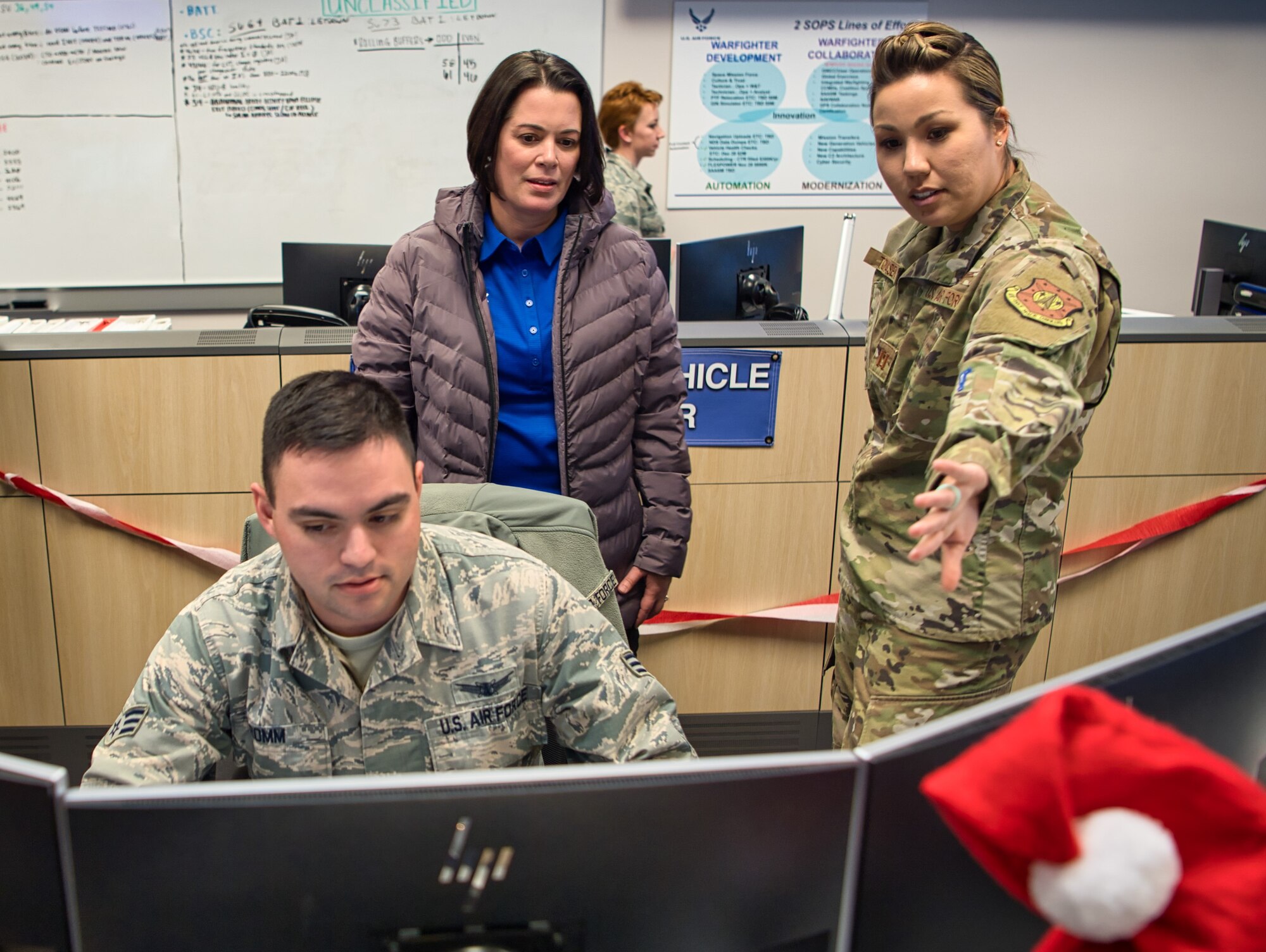 Capt.  Angela Tomasek, 2nd Space Operations Squadron engineering flight commander, briefs retired Col. Nicole Malachowski, while Senior Airman Sean Romm, 2nd SOPS space systems operator, mans a control station, while on a tour of the 2nd SOPS floor during her visit to Schriever Air Force Base, Colorado, Dec. 19, 2019. Malachowski, the first female Thunderbird pilot, spent 21 years in the Air Force. After being medically discharged due to a life threatening tick borne illness in 2017, Malachowski decided to use the pain and lessons learned to bring hope to thousands through her motivational speeches focused on the value and importance of resilience, resurgence and re-invention. (U.S. Air Force photo by Katie Calvert)