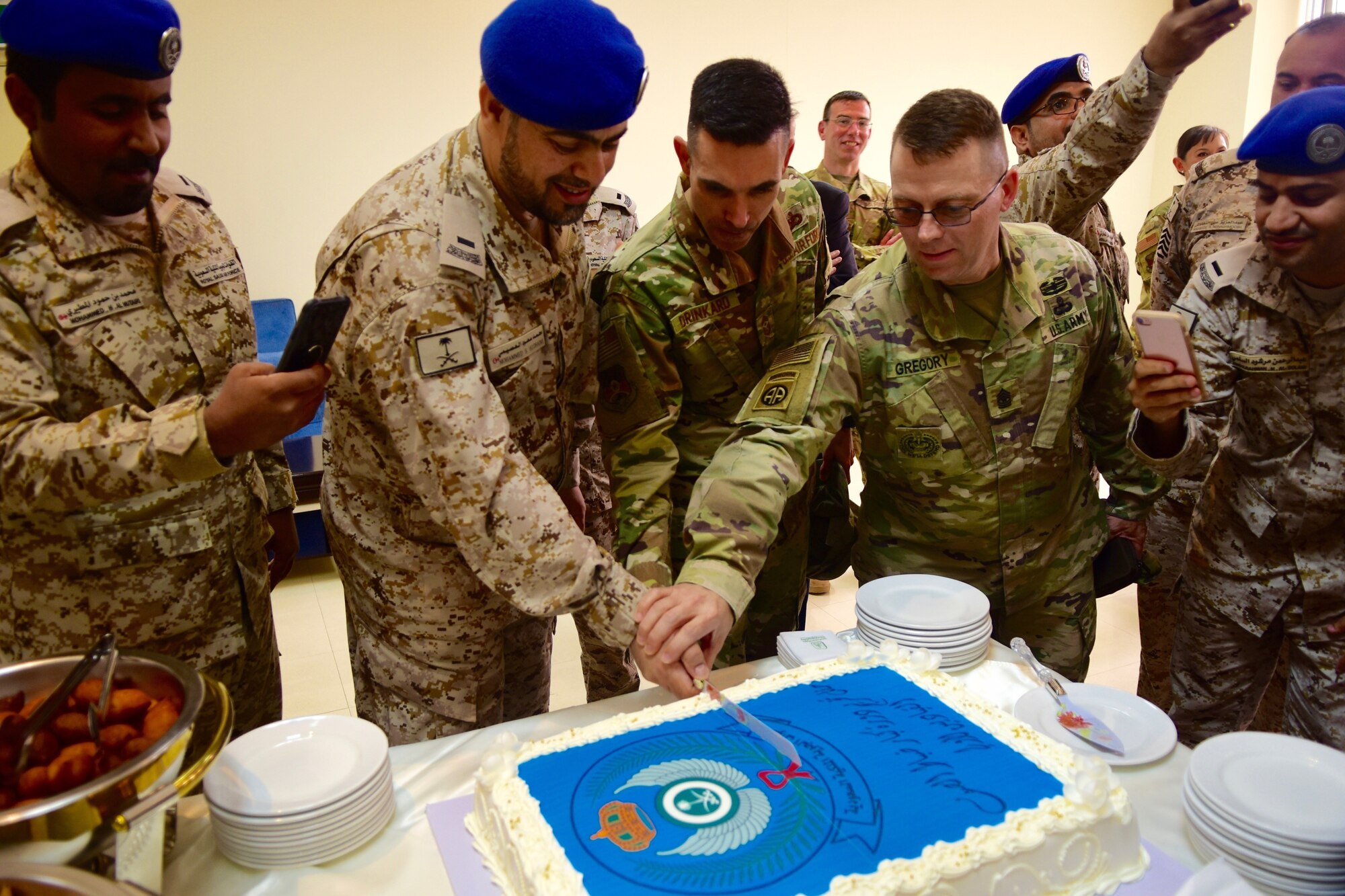 U.S. Air Force Chief Master Shawn Drinkard, U.S. Air Forces Central Command command chief, joins U.S. Army Sergeant Major Charles Gregory, U.S. Military Training Mission- Kingdom of Saudi Arabia senior enlisted advisor, and Royal Saudi Air Force Chief Master Sgt. of RSAF Mohammed Alosaimi, in cutting a cake after a graduation ceremony here, Dec. 11, 2019.