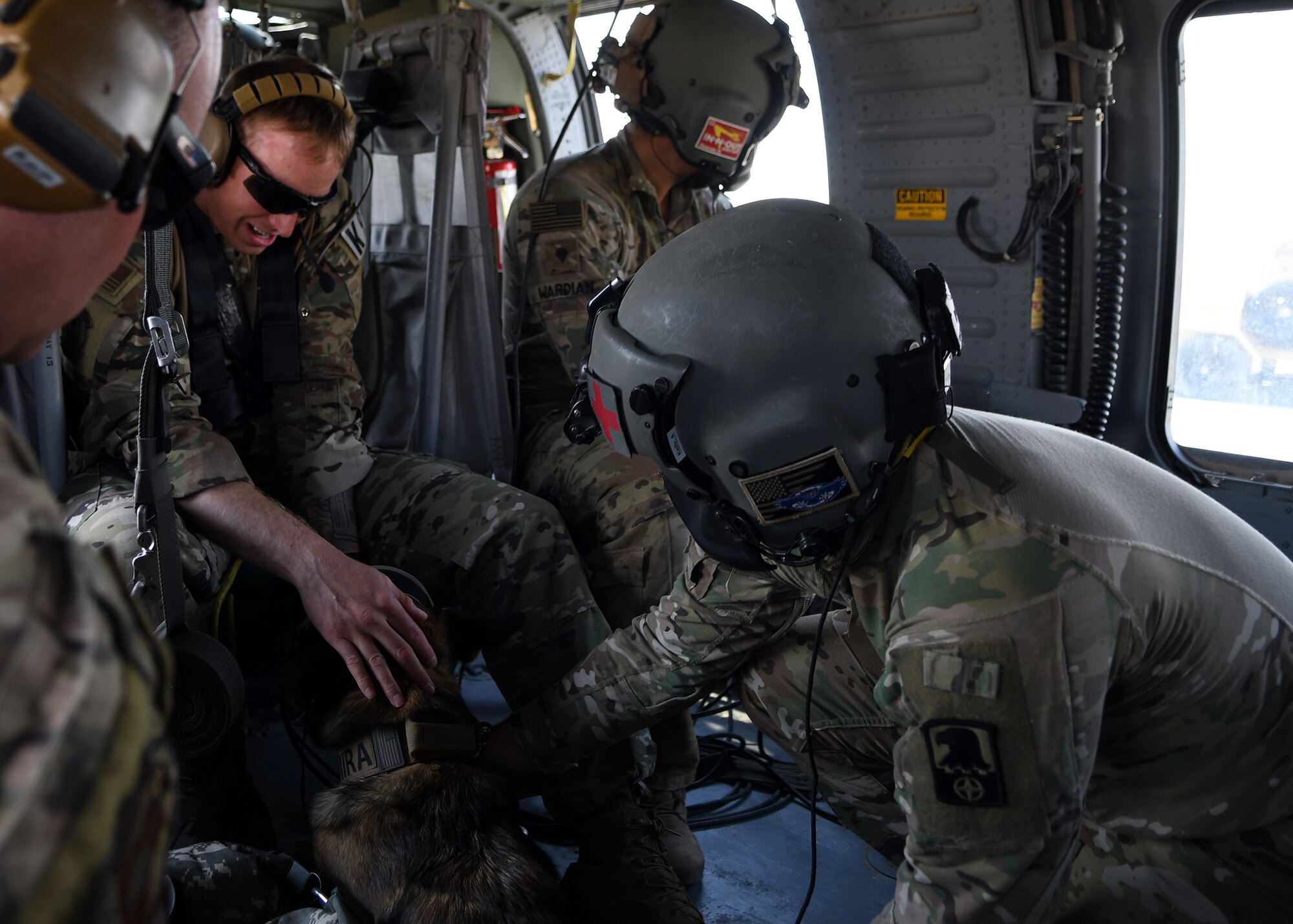 U.S. Air Force Staff Sgt. Bryan Abercrombie, 378th Expeditionary Security Forces Squadron K-9 handler, and U.S. Army Specialist Andrew Kelly, Golf Company General Support Aviation Battalion flight medic, comfort Mira, 378th ESFS military working dog, during helicopter acclimation training Nov. 27, 2019, at Prince Sultan Air Base, Saudi Arabia.