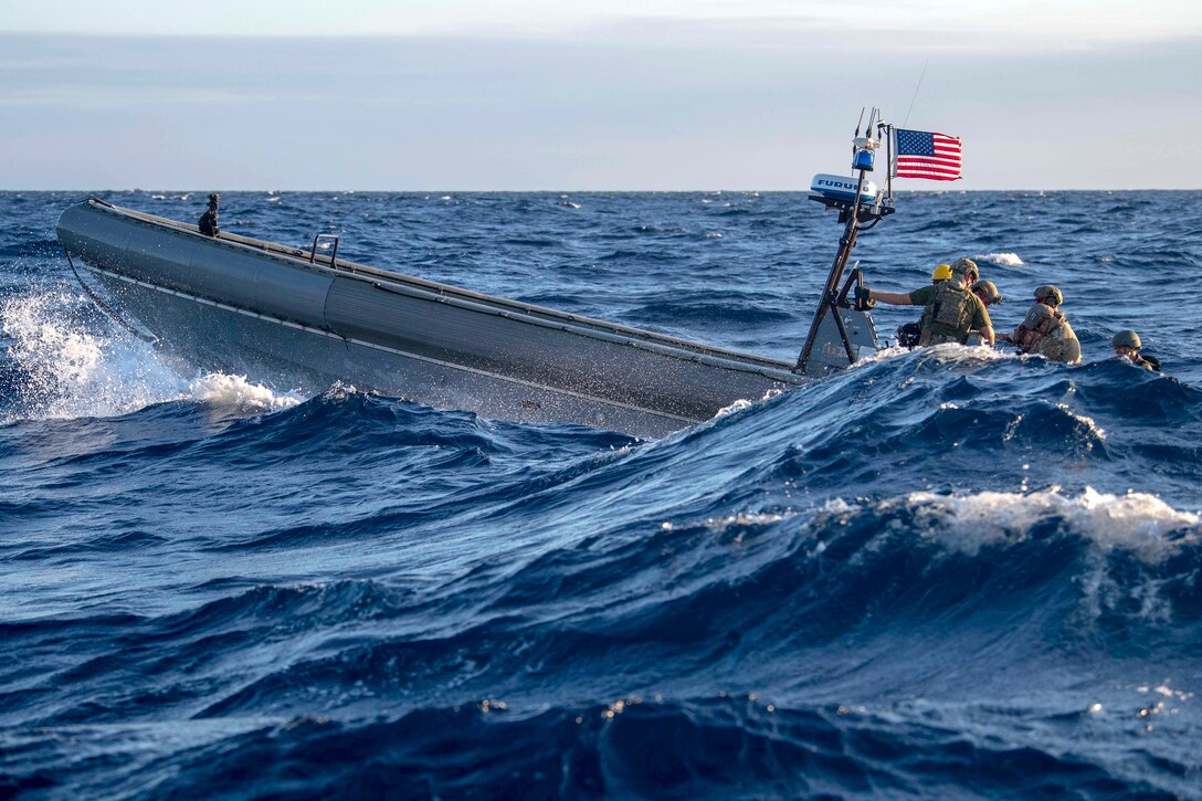 Sailors and Coast Guardsmen steer a small boat through waves in a blue sea.