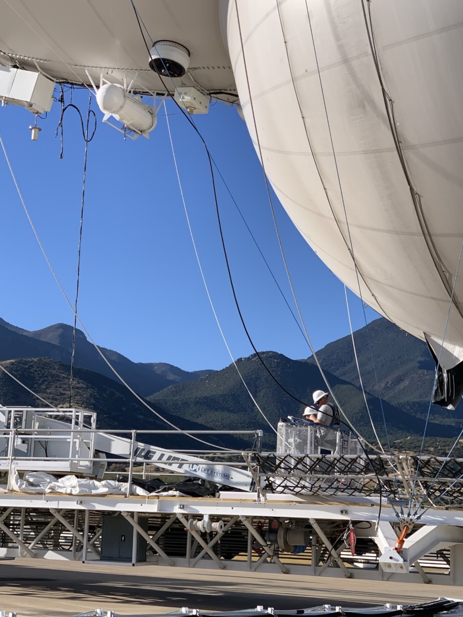 Image is a tethered aerostat radar system (TARS) device being optimized by personnel.