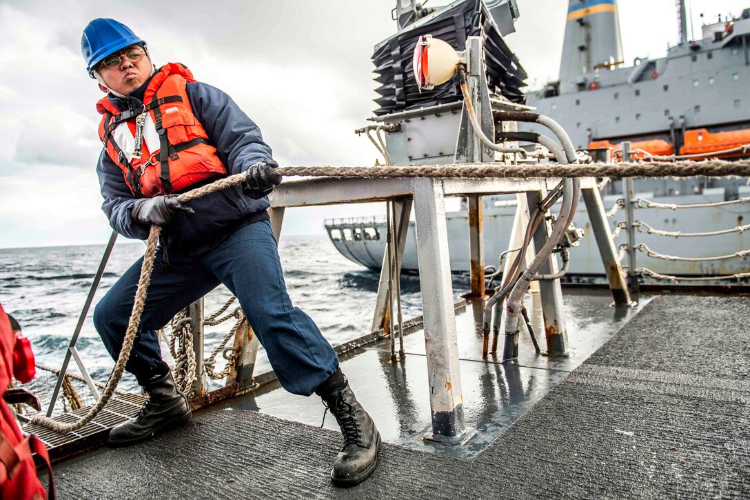 A sailor pulls a line on a ship's deck.