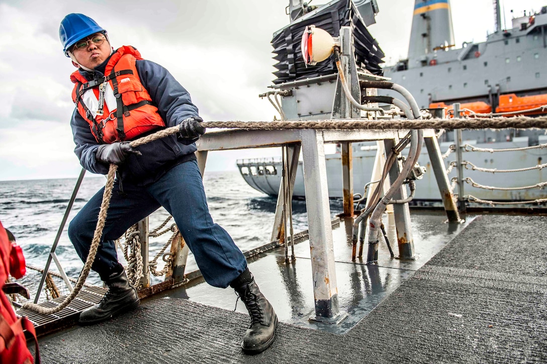 A sailor pulls a line on a ship's deck.