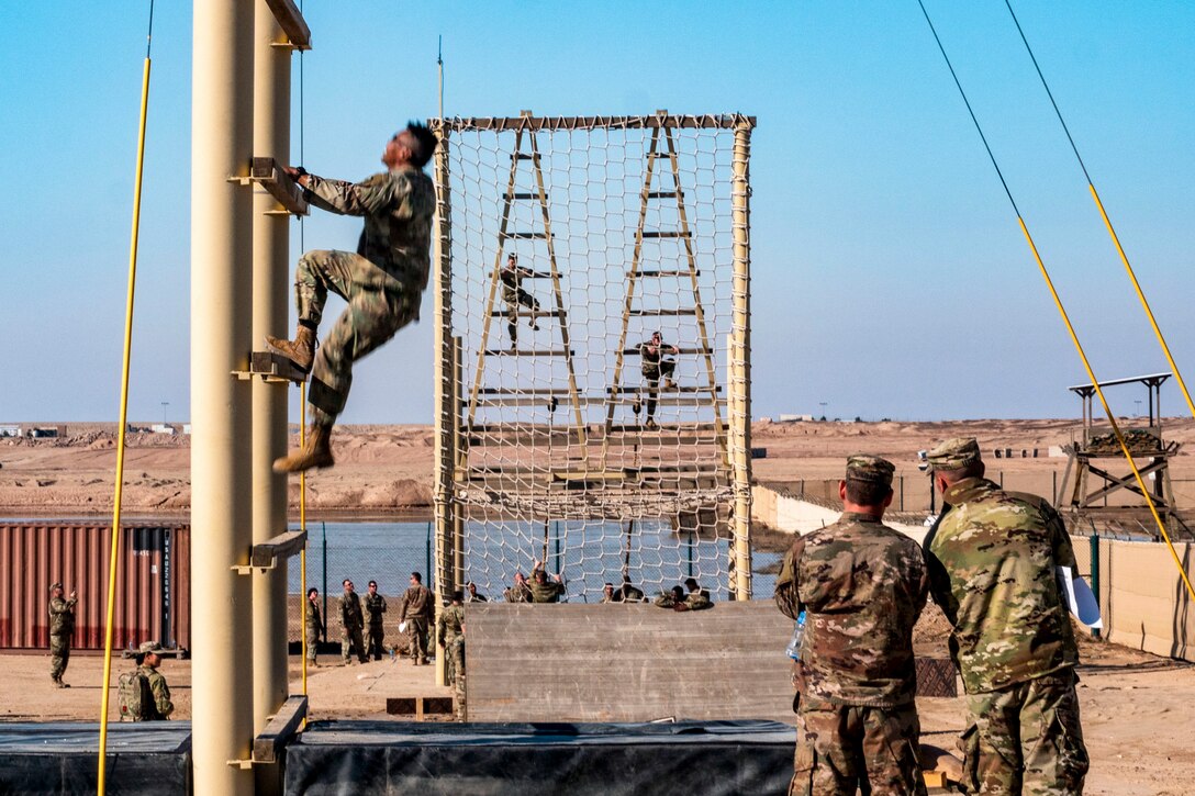 Soldiers climb obstacles as troops watch on the ground.