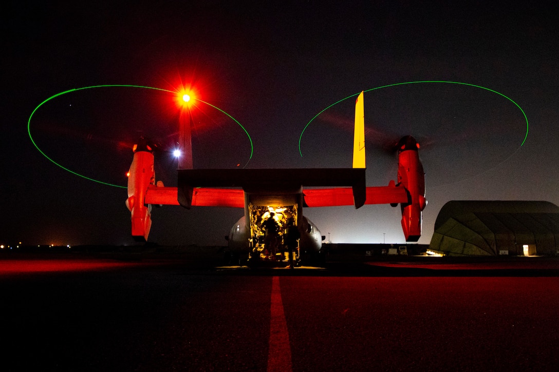 Marines are illuminated inside an open aircraft on a dark flightline.
