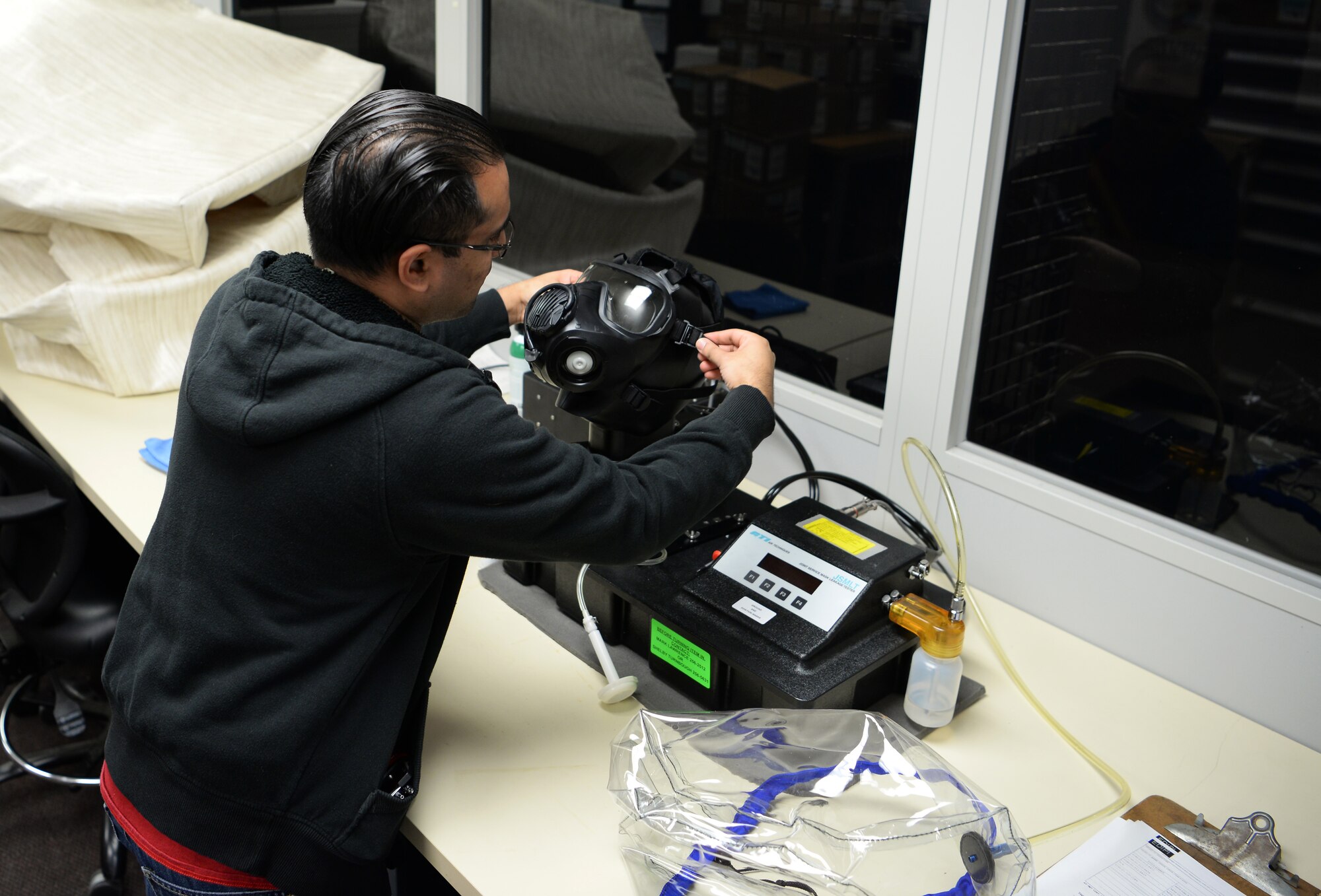 Christopher Greene, 375th Logistic Readiness Squadron individual protective equipment specialist, adjusts the straps on an M50 gas mask while it is placed over a Joint Service Mask Leakage Tester, Jan. 28, 2019, at Scott Air Force Base, Illinois. The gas mask tester ensures that the gas mask is able to get a good seal while someone is wearing it. This ensures harmful chemicals cannot seep through the mask while it is on the wearer.