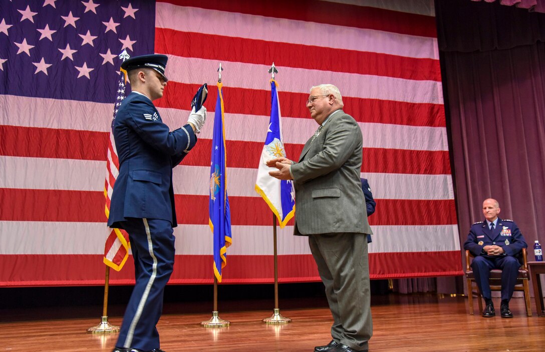 Senior Airman Beaux Hebert, Columbus Air Force Base Honor Guard, hands Richard “Sonic” Johnson, former 14th Flying Training Wing Public Affairs chief, a folded American flag during Johnson’s retirement ceremony at the Kaye Auditorium Jan. 25, 2019, on Columbus AFB, Mississippi. (U.S. Air Force photo by Melissa Doublin)