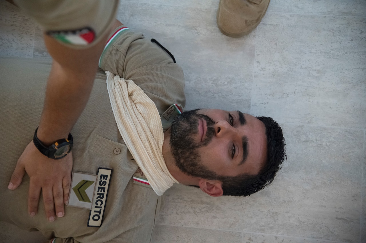 A man lies on ground with dressing around his neck and shoulder.