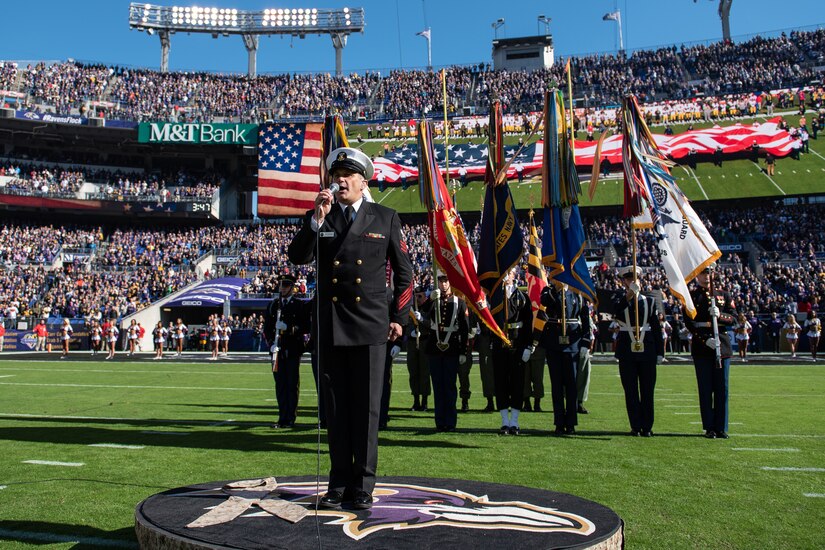 A sailor sings the national anthem at football game.