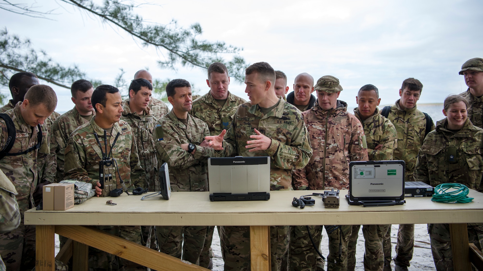 Service members from the Joint Communications Support Element and the British Army’s 30th Signal Regiment gather around U.S. Army Staff Sgt. Kevin Shells (center), a JCSE systems team chief, at Beer Can Island, Fla. Jan. 30, 2019, as he demonstrates how to set up and utilize communications equipment in a deployed environment with no power source. As part of the Cobb Ring exercise, the two nations trained together to demonstrate capabilities with coalition partners and strengthen relationships.