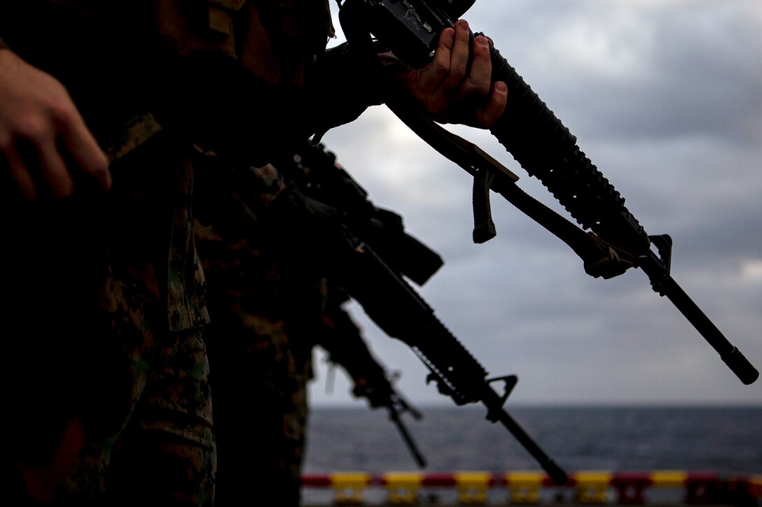 Marines hold guns on a navy ship.