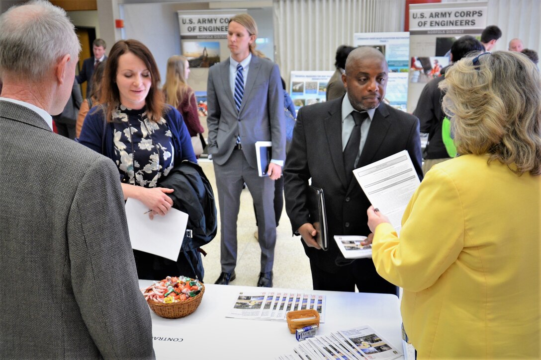 group of well-dressed attendees are waiting to talk to man and woman behind a table while holding their resumes and other documents