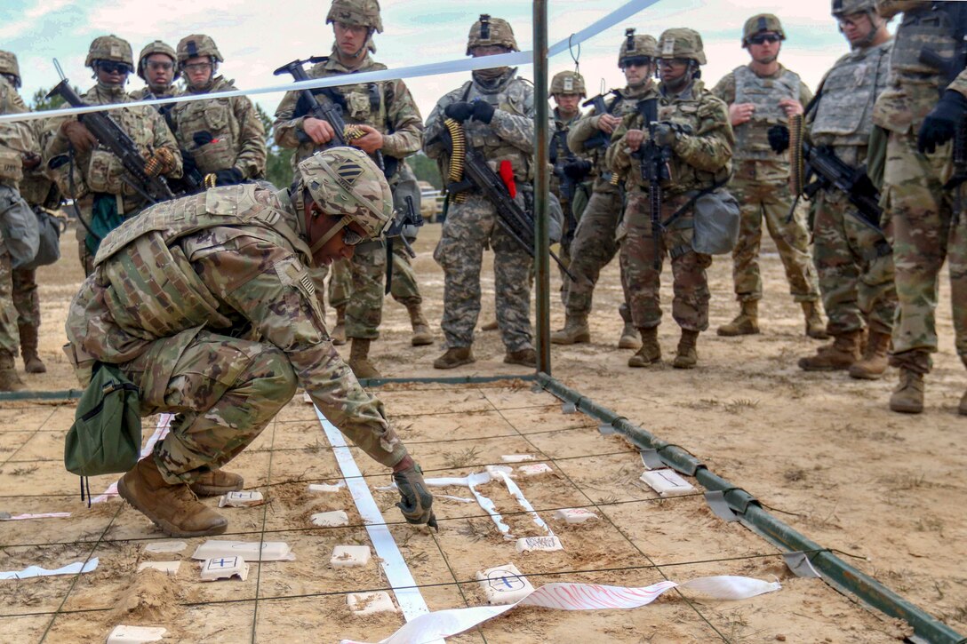 A solider demonstrates inert crater charges on the ground with a grid.