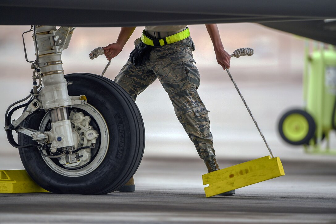 An airman removes wooden bumpers from the wheels of a fighting jet.