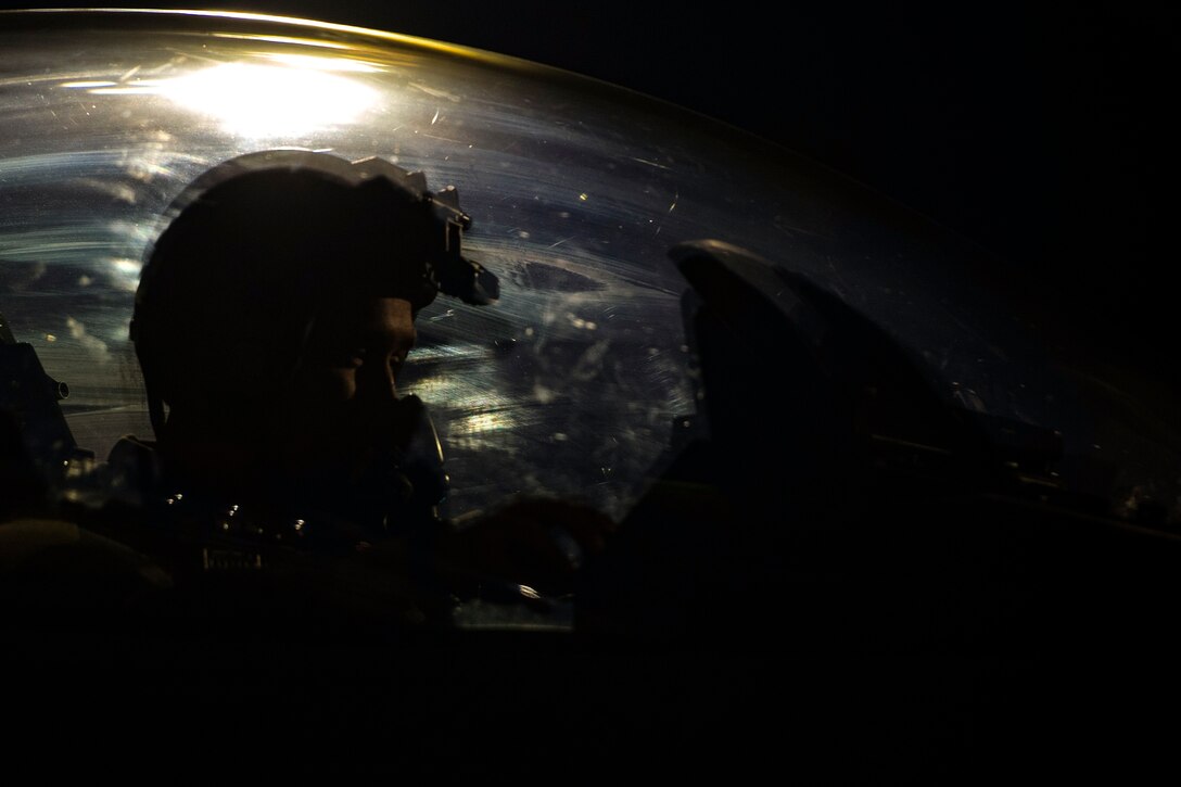 A pilot adjusts his face mask while sitting in a cockpit.
