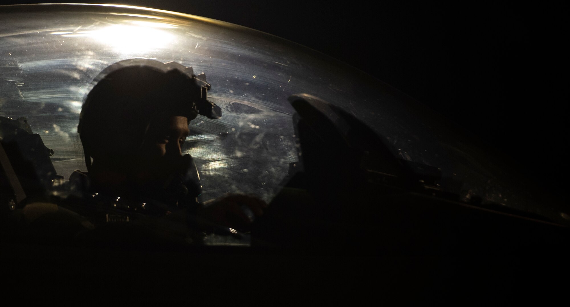 A pilot sits in the cockpit of an F-16 fighting Falcon fighter jet at night.