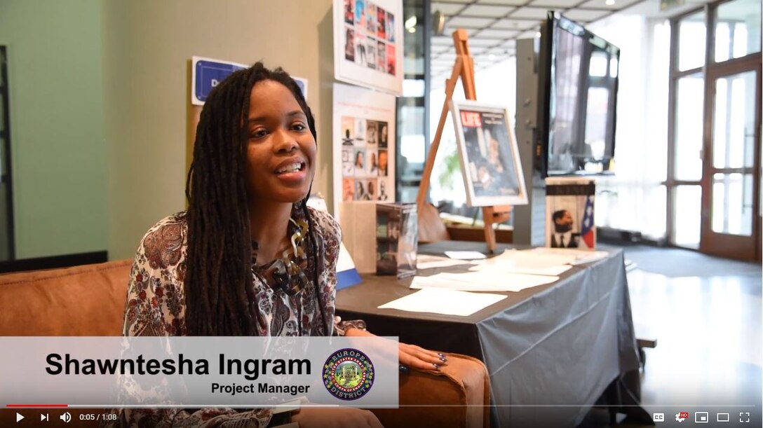 Woman sits in a chair in a lobby, in front of posters and pamphlets honoring Dr. Martin Luther King Jr.