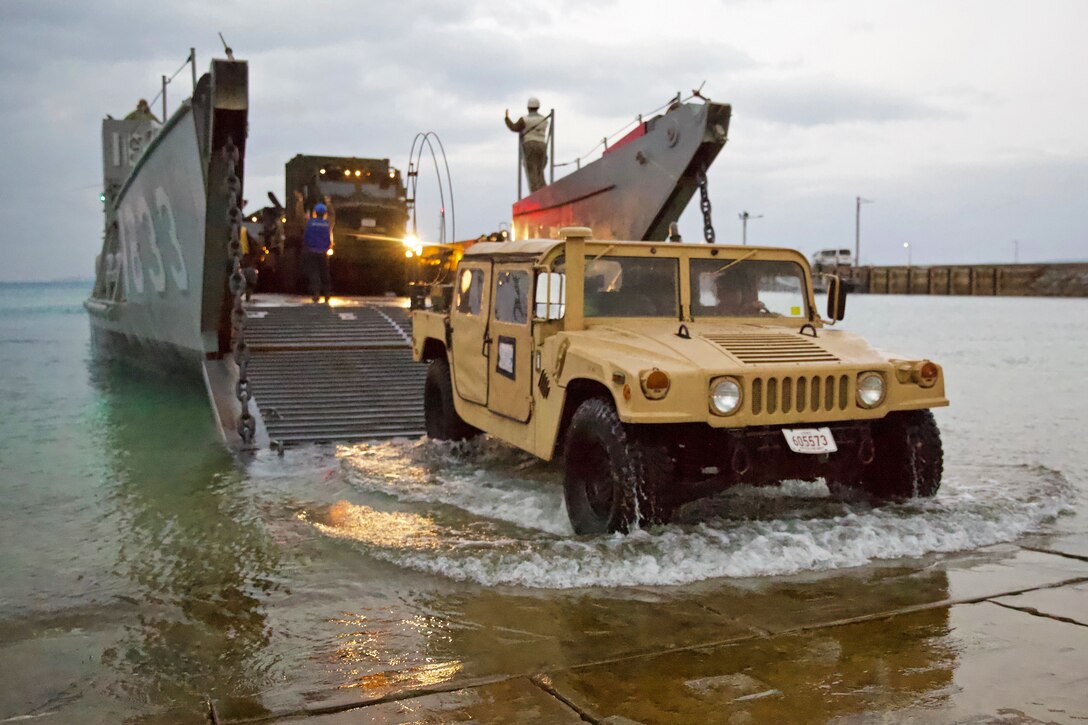 A Humvee rolls onto land from a landing craft vehicle.