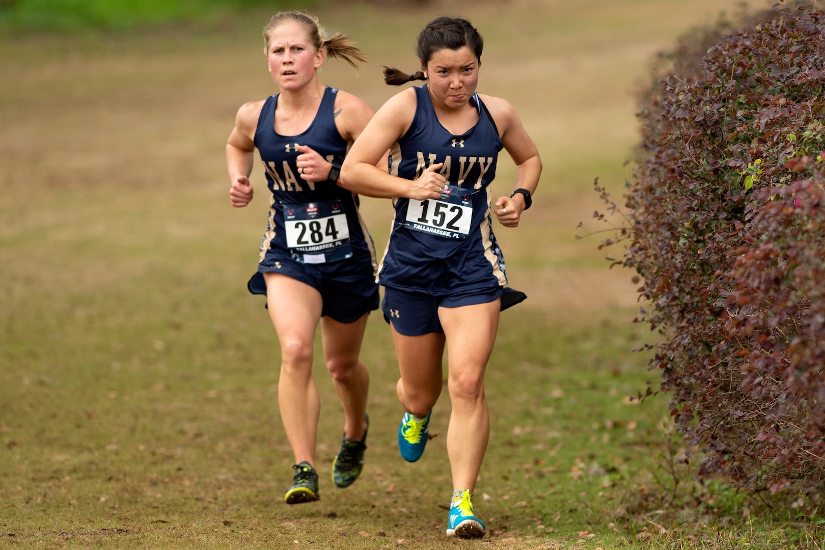 Two athletes wearing race numbers jog on flat terrain.