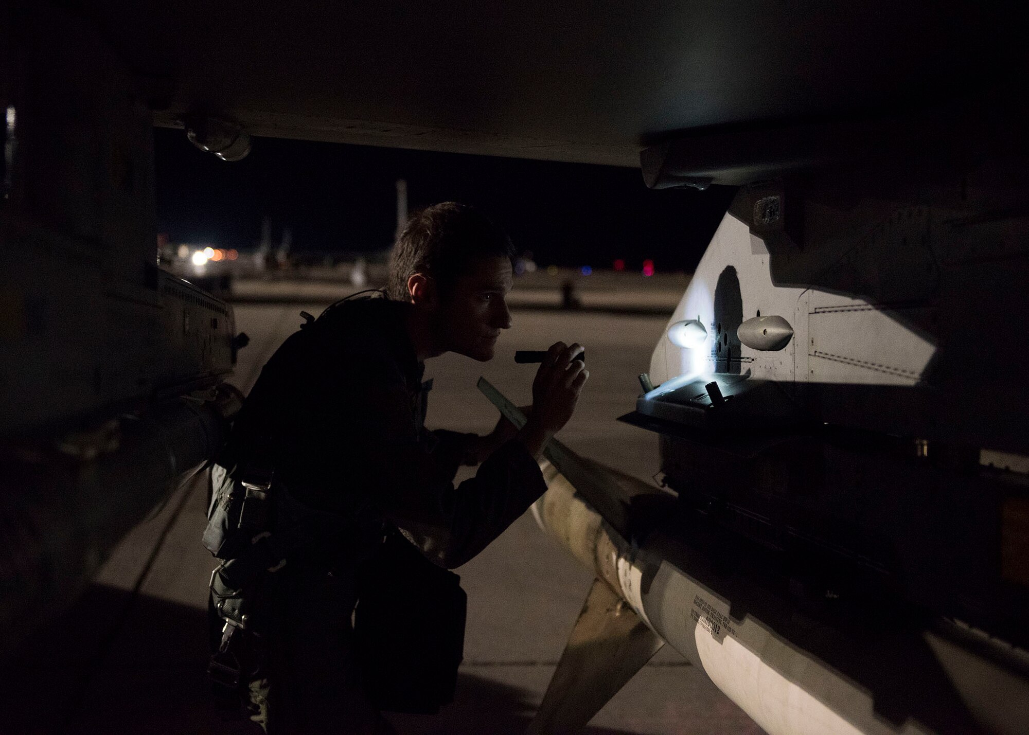 A pilot uses a flashlight to inspect the wing of an F-16 Fighting Falcon fighter jet.