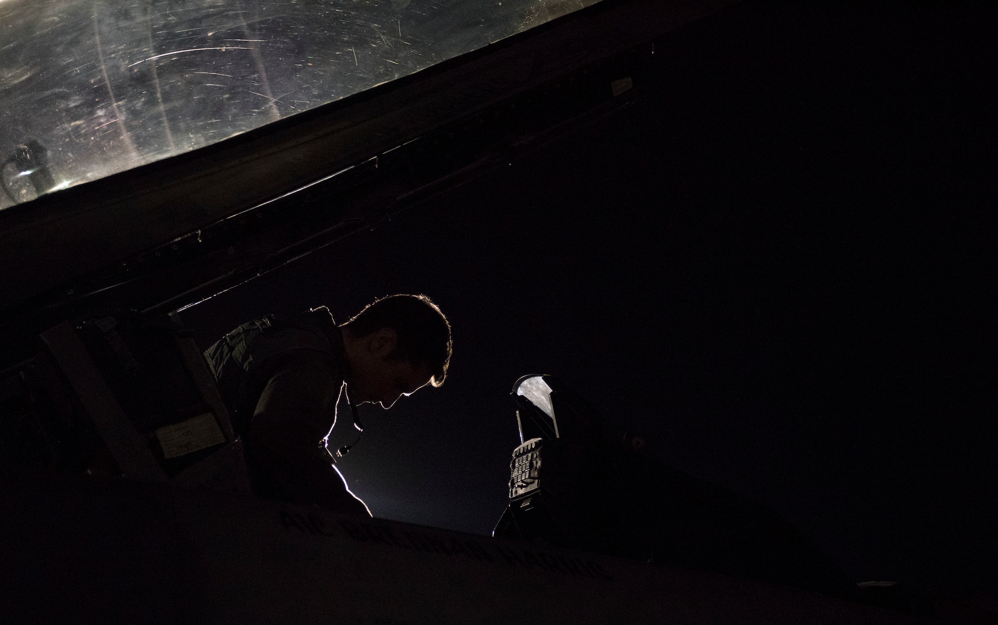 A pilot sits in the cockpit of an F-16 Fighting Falcon fighter jet at night.