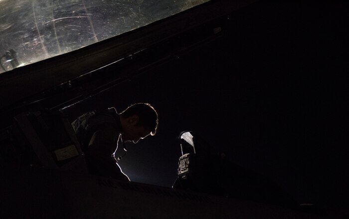 A pilot sits in the cockpit of an F-16 Fighting Falcon fighter jet at night.