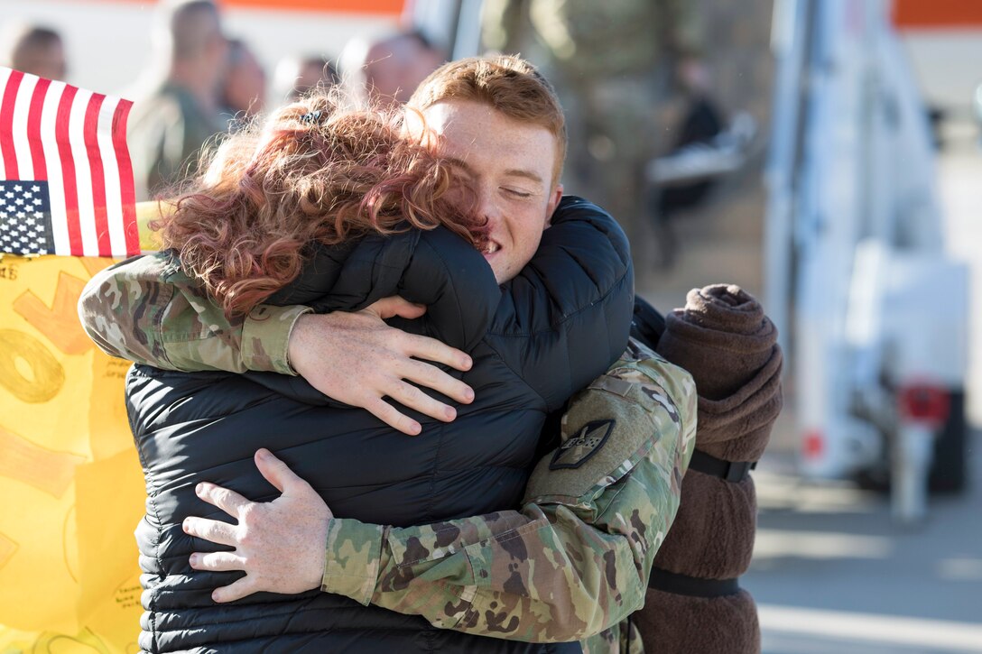 A soldier hugs a woman on a flightline.