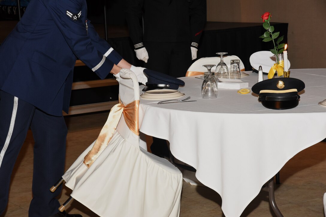 A Joint Service Color Guard member sets an Air Force cover on an empty table reserved to honor missing comrades in arms at the Annual Awards Ceremony at the McNeese Convention Center, San Angelo, Texas, Feb. 1, 2019. The table was set for five, one seat from each branch of service, symbolizing their inability to share the evening’s festivities.  (U.S. Air Force photo by Airman 1st Class Abbey Rieves/ Released)