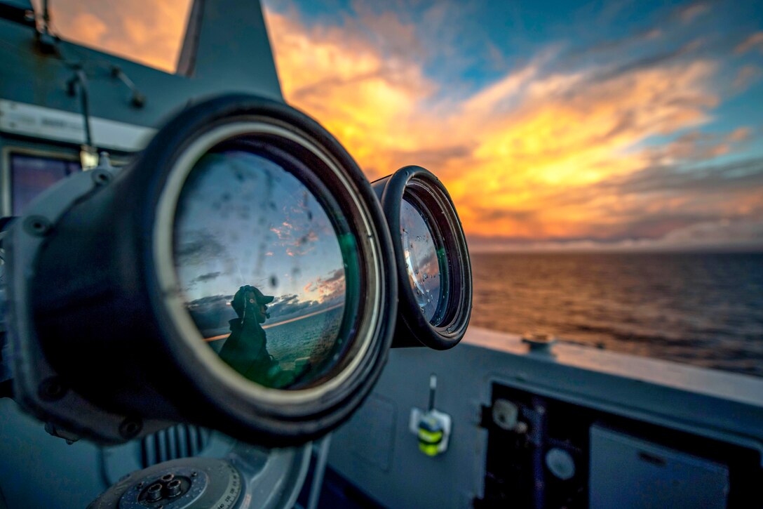 A sailor is reflected in the lens of optical equipment on a ship.