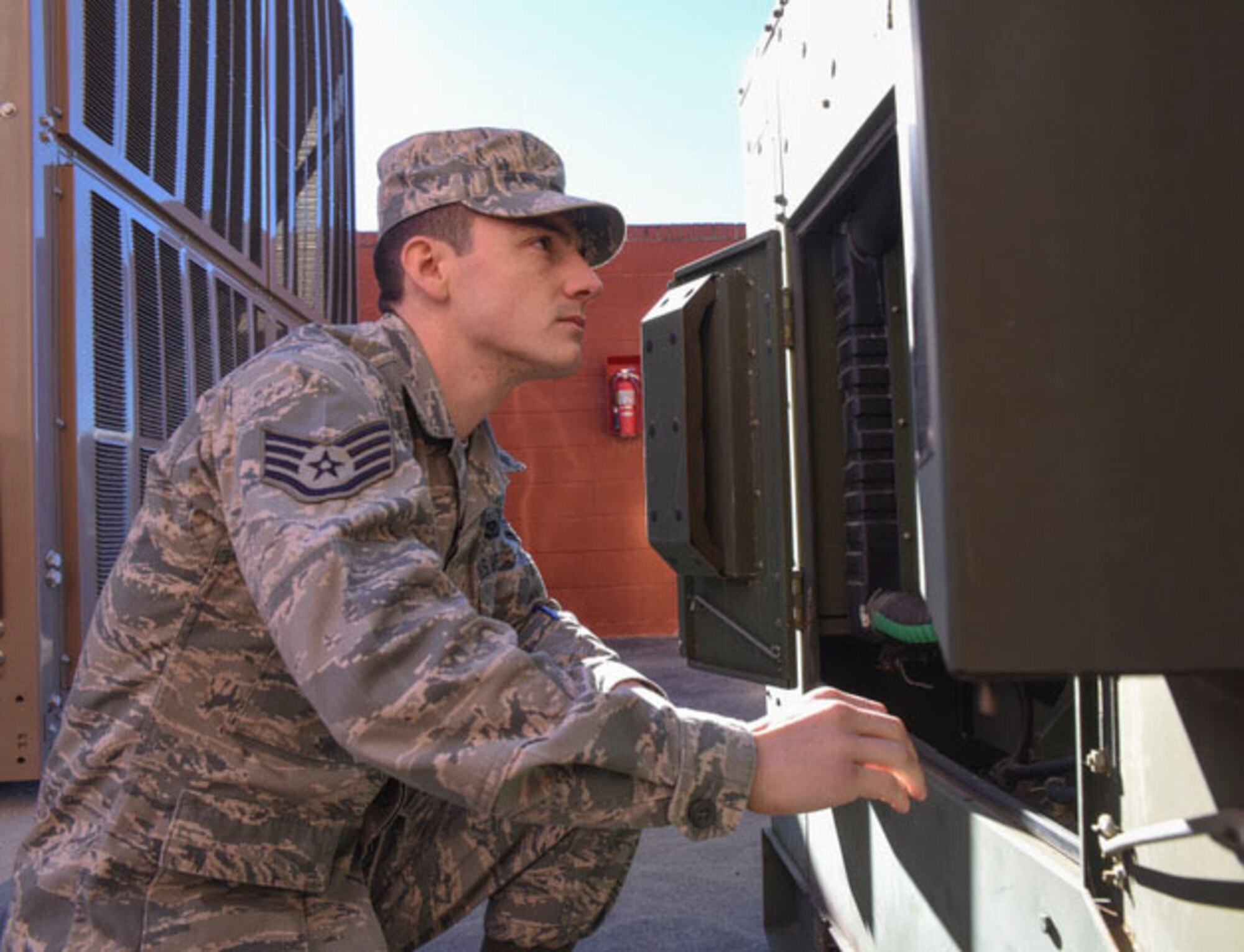 A man crouches in front of a metal machine.