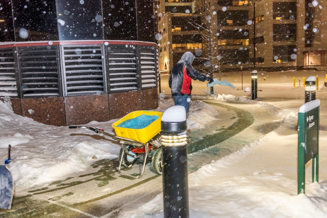 Guy spreading salt on sidewalks while it's snowing