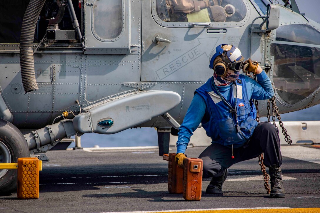 A sailor removes securing gear from a helicopter on the deck of a ship.