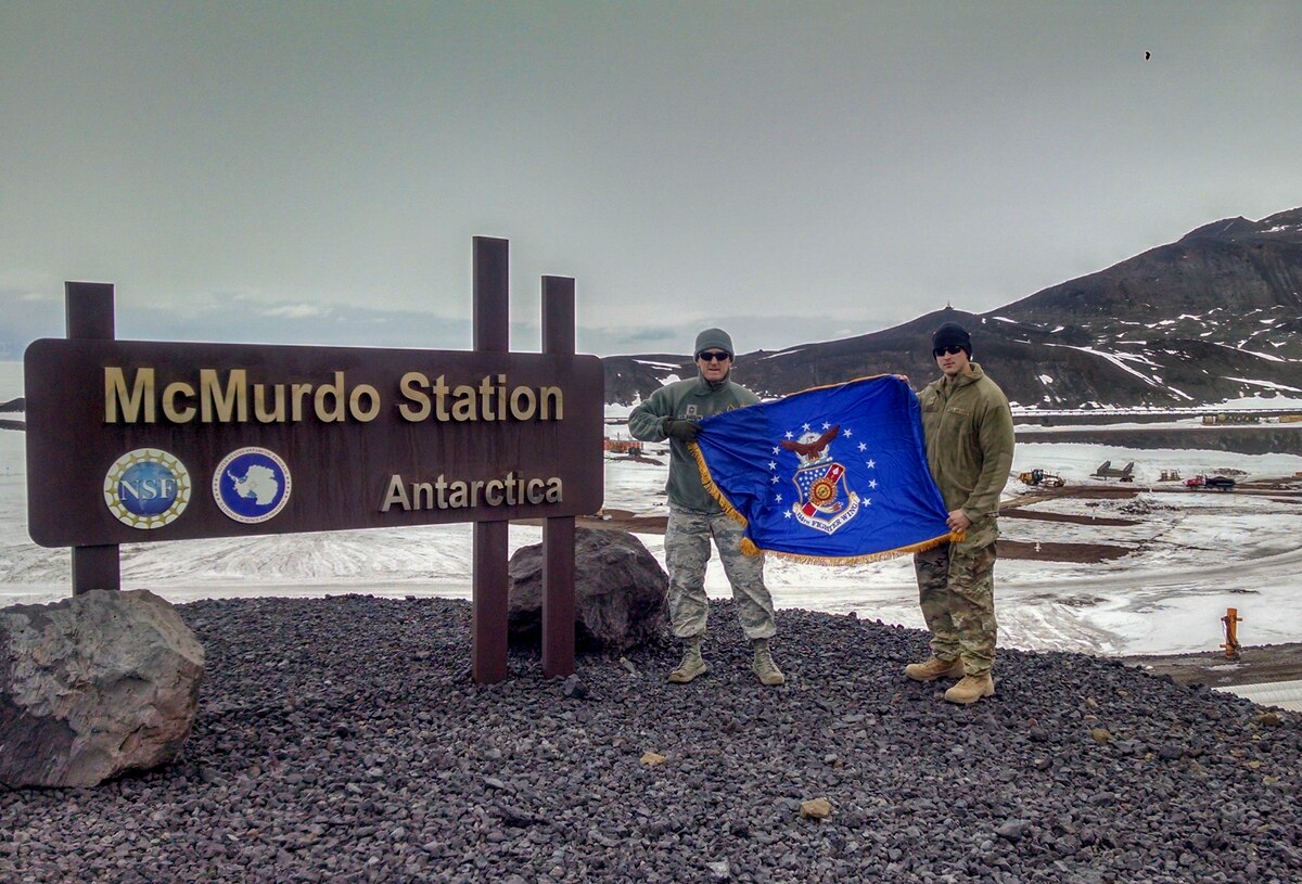Chief Master Sgt. Troy Erlandson, 114th Fighter Wing occupational safety manager, holds the South Dakota Air National Guard flag with another Airman during his trip to McMurdo Station, Antarctica, where he worked directly for Joint Force Antarctica to support their research mission.