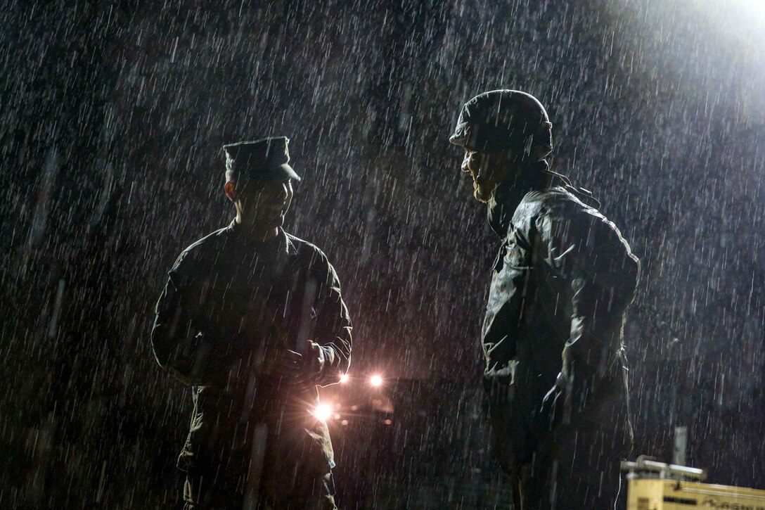 Two Marines talk in the night rain.