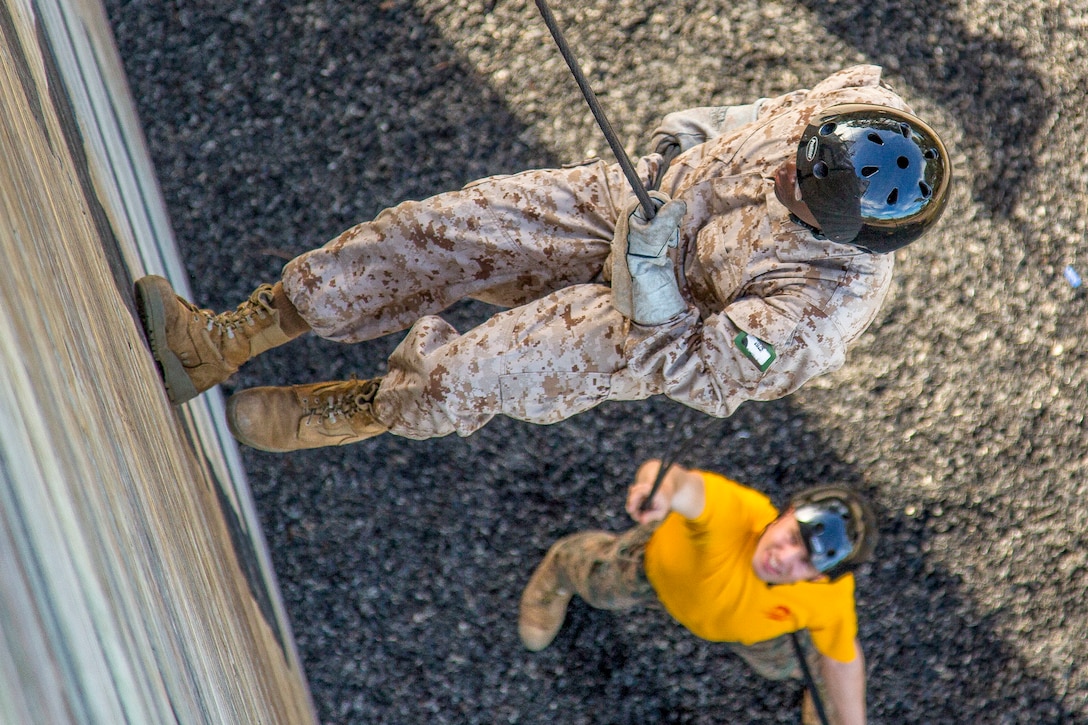 A Marine rappels down a wall while a trainer waits at the bottom.