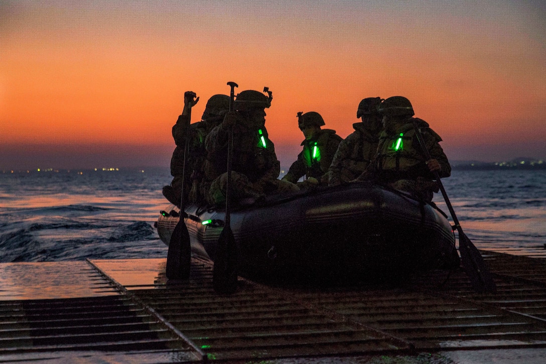 Marines sit in a rubber boat about to head out to sea.