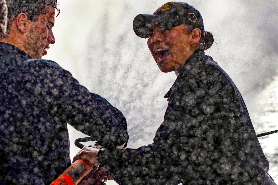 A sailor trains another sailor in how to use a firehose.