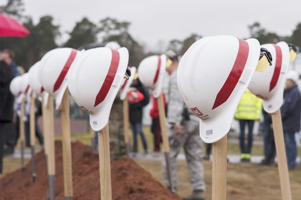 Hard hats balance on top of shovels sticking out of the ground.