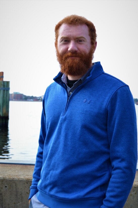 man with blue sweater poses in front of water