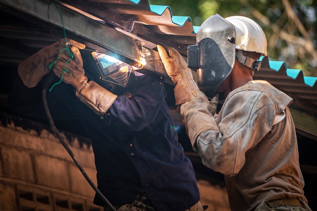 Two sailors welding steel beams.