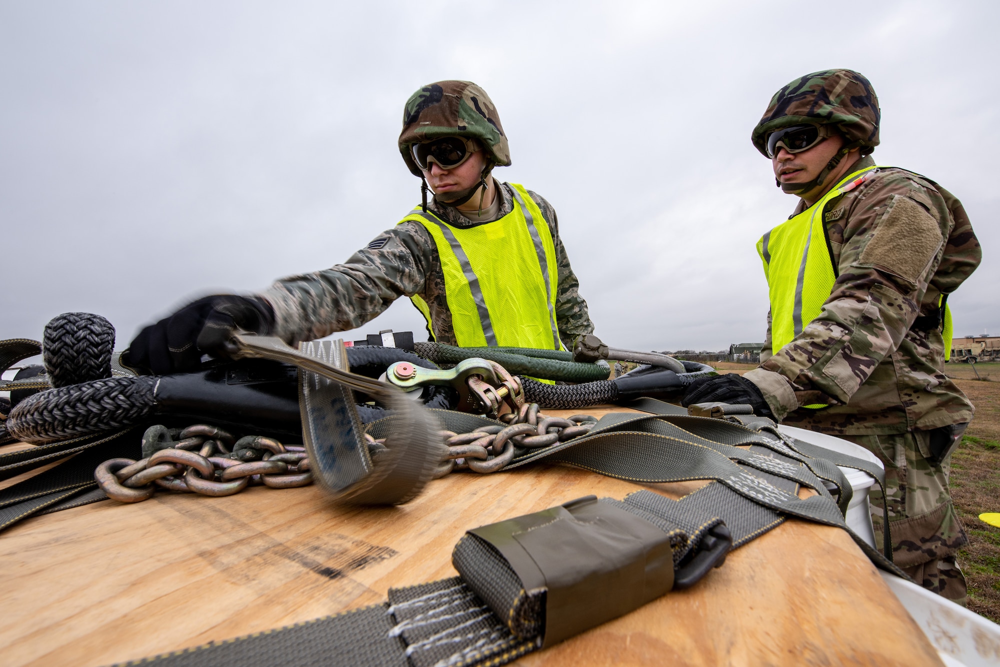 Senior Airman Timothy Watson, left, and Staff Sgt. Jose Frias, aerial transportation technicians, 26th Aerial Port Squadron, prepare to secure a 2,000-pound piece of cargo to a UH-60 Black Hawk helicopter flown by Soldiers from the Texas Army National Guard, Company C, 2-149 Aviation Regiment, during a sling load training event on Feb. 1, 2019, at Martindale Army Airfield, San Antonio, TX.